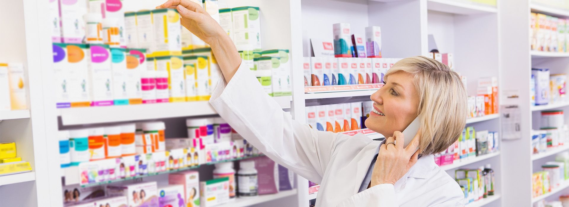 Ein Apotheker in einem weißen Laborkittel stellt ein Produkt auf ein hohes Regal in einer bunten Apotheke, die mit verschiedenen Medikamenten gefüllt ist.
